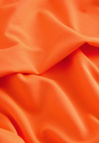 Tissu lisse orange vif avec des plis doux et des ombres légères mettant en valeur la texture et le drapé.