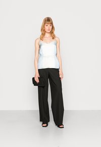 Camisola de cetim azul em gradiente com alças finas, cintura ajustada, combinada com calças largas pretas e uma clutch preta. Textura suave, design casual.