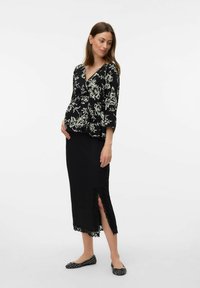 Blouse noire à fleurs avec des manches trois-quarts, assortie à une jupe noire avec une fente sur le côté et une bordure en dentelle, complétée par des ballerines à motifs.