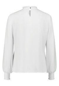 Blouse blanche à manches longues avec poignets smockés, tissu texturé, petite ouverture dans le dos et fermeture par bouton à l'encolure.