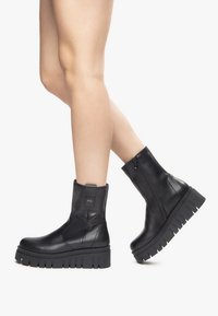 Bottines noires en cuir avec une semelle épaisse, dotées d'une fermeture éclair sur le côté, d'une languette à l'arrière et d'un motif de sculpture texturé.