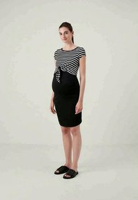 Gestreiftes Schwarz-Weiß-Oberteil mit Schleifen vorne und kurzen Ärmeln, kombiniert mit einem figurbetonten schwarzen Rock und schwarzen Riemchensandalen.