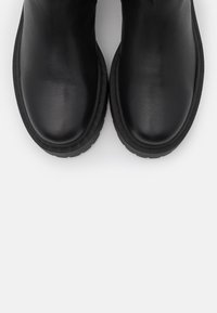 Svarta läderankelboots med rundade tår, gummisulor och minimal sömnad. Slät textur med en lätt lyster.