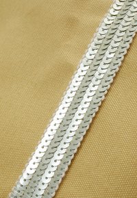 Närbild av beige tyg med tre vertikala rader av glänsande silverpaljetter sydda i parallella linjer.