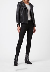 Svart läderbikerjacka med dragkedja vid ärmslut, bärs över en vit t-shirt, i kombination med svarta tajta jeans och ankelstövlar.