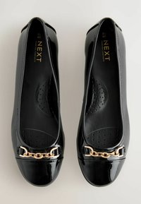 Ballerines en cuir verni noir avec un bout rond, un accent en chaîne dorée à l'avant et une semelle intérieure rembourrée avec des perforations.