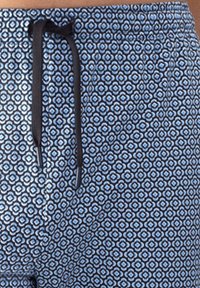 Blauwe bedrukte shorts van lichtgewicht stof, voorzien van een geometrisch patroon in donkerblauw en wit, met een zwarte trekkoordsluiting.