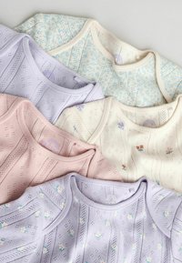 Fem babybodier i pastelfarver med delikate strikkemønstre og små blomsterprints, arrangeret i overlap på en lys baggrund.