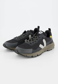 Scarpe da trekking nere con tomaia in rete, accenti in gomma, lacci riflettenti e suola testurizzata nei toni grigio e oliva. Dettaglio del tallone giallo distintivo.