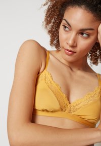 Bralette amarelo com renda, feito de um tecido suave e macio, com alças ajustáveis; apresenta um design de copo triangular.