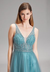 Abito da sera blu acquamarina con scollatura a V profonda e corpetto ricamato. Gonna in tulle fluente e dettagli intricati in perline creano un design elegante e testurizzato.