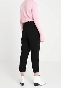 Pantaloni neri a sigaretta con risvolti, abbinati a un maglione rosa chiaro. Il modello indossa stivaletti bianchi alla caviglia con tacco grosso.