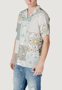 Camisa de manga corta con cuello y diseño de patchwork que presenta patrones geométricos en verde, gris y naranja. Hecha de tejido ligero.
