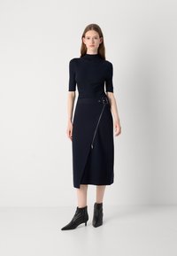 Robe marine avec un haut ajusté en maille côtelée, des manches courtes et un ourlet asymétrique. Elle est dotée d'une ceinture avec des garnitures en métal et d'un détail de fermeture éclair diagonale.