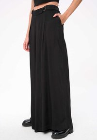 Zwarte wijde broek met hoge taille, voorzien van een riem met een metalen gesp en zijzakken, gemaakt van gladde stof.