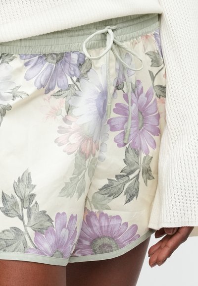 Pantalones cortos florales en tejido ligero con flores en tonos morados y rosas pastel sobre un fondo crema. Cintura elástica con cordón ajustable.