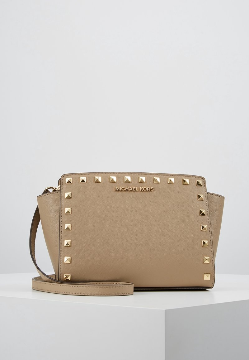 Beżowa torebka Michael Kors z złotymi ćwiekami wzdłuż jednej strony, z zamkiem błyskawicznym i odczepianym paskiem. Wykonana z ustrukturyzowanej skóry.