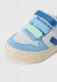 Sinine ja helesinine tennis, millel on segu tekstuursed naha ja suede, kolm Velcro-rihma ja aukudega toe kast.