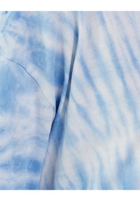 Bavlněná košile s jemným modrým tie-dye vzorem, s hladkým povrchem a měkkou tkaninou, viditelné švy na rameni.