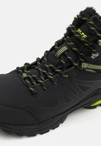 Black hiking boot with green accents, textile upper, textured design, laces, and cushioned collar. Features rugged outsole for traction.