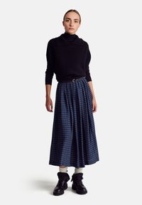 Black ribbed turtleneck sweater with a folded collar, paired with a long blue patterned skirt. Fabric texture is soft; black sturdy ankle boots complete the outfit.