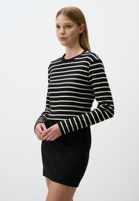 Maglietta a maniche lunghe a righe bianche e nere con scollatura tonda, abbinata a una mini gonna nera aderente. Tessuto liscio, design casual.