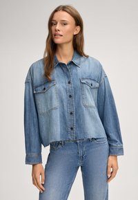 Denim jacket with a cropped design, light blue color, button closure, two chest pockets, and cuffed long sleeves.