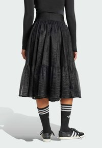 Black tiered skirt with a textured finish, elastic waistband, and layered ruffles. Worn with black socks featuring white stripes and sneakers.