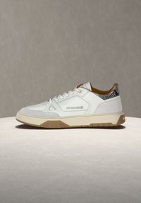 Λευκό sneaker χαμηλού ύψους με μπεζ σόλα, λεπτομέρεια από δέρμα φιδιού στη φτέρνα και "roberto cavalli" εγχάραξη στο πλάι.