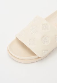 Sandale slip-on crem cu un superior texturat, cu modele florale embossate și o talpă netedă, rotunjită pentru confort.