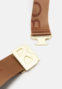 Cintura in tessuto marrone con una fibbia metallica dorata lucida che presenta una lettera "B" prominente. La cinghia include un logo impresso tono su tono.