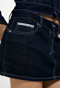 Σκούρα μπλε μίνι φούστα τζιν με άσπρες ραφές και μια μικρή ετικέτα Juicy Couture Jeans στην πίσω τσέπη.