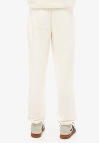 Crème-kleurige sweatpants met elastische boorden, gemaakt van zachte stof. Draag ze met lichtgrijze schoenen met bruine zolen en multicolo-accenten.
