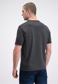 Tamsiai pilka trumpomis rankovėmis marškinėliai su apvalia iškirpte, lygiu audiniu ir mažu logotipo akcentu kairėje rankovėje. Kasdienis modelis.