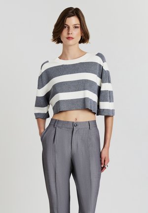 Pull court rayé gris et blanc avec des manches larges, associé à un pantalon plissé gris clair avec fermeture à bouton et poches latérales.