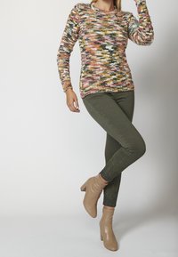Kolorowy sweter z dzianiny w odcieniach różu, żółci, zieleni i bieli; zestawiony z oliwkowymi skinny spodniami i beżowymi botkami na obcasie.