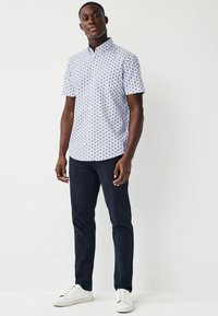 Maglietta a maniche corte di colore azzurro chiaro con un motivo di piccoli triangoli blu scuro, abbinata a pantaloni blu navy e sneakers bianche.