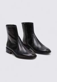 Botines de cuero negro hasta el tobillo con un acabado elegante y suave, punta afilada y cremallera lateral. Tacón bajo y cuadrado con detalles de costura mínimos.