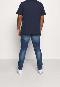 T-shirt bleu marine et jeans bleus, design ajusté avec une texture lisse. Les jeans présentent un style classique à cinq poches et un léger délavage. Baskets blanches.