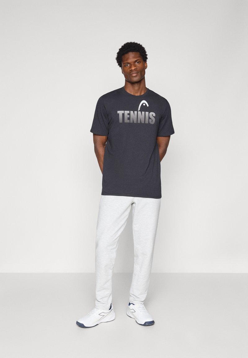 Camiseta gris oscura con estampado y logotipo en blanco de "TENNIS", combinada con pantalones de chándal gris claro y zapatillas blancas. Ajuste suave y casual.