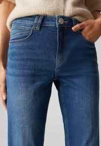 Blauwe denim jeans met een getailleerd ontwerp, voorzien van een klassieke knoopsluiting, voorzakken en subtiele stiksels aan de zijkanten.