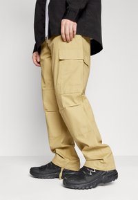 Beige cargo bukser med flere lommer, lavet af slidstærkt stof. Pasformen er afslappet med en glat overflade og forstærkede syninger.