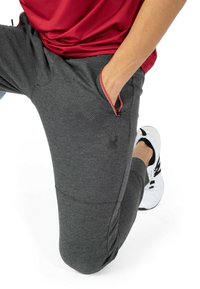 Grå træningsbukser med tekstureret stof, slim fit og røde lynlåse detaljer. Har sidelommer og et logo på låret.