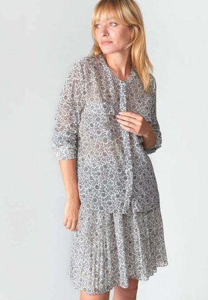 Abito lungo e trasparente con maniche lunghe, decorato con un motivo floreale in grigio e bianco, dotato di una chiusura frontale con bottoni e gonna plissettata. Tessuto leggero e testurizzato.