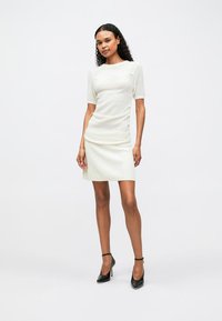 Λευκό πλεκτό τοπ με κοντά μανίκια, συνδυασμένο με λευκή μίνι φούστα με ρίγες. Μαύρες στιλέτο γόβες ολοκληρώνουν το ντύσιμο. Λείο ύφασμα, εφαρμοστή σχεδίαση.