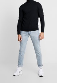 Schwarzer Rollkragenpullover, gestrickter Stoff, figurbetontes Design. Kombiniert mit hellblauen Jeans und weißen Sneakers mit schwarzen Akzenten.