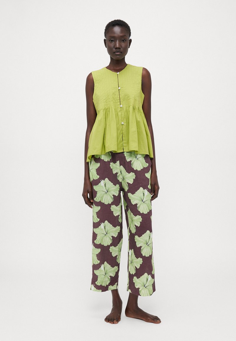 Green sleeveless top with a button front and gathered waist, paired with wide brown pants featuring large light green floral patterns.