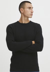 Fekete kötött pulóver texturált mintával, kerek nyakkal és bordázott mandzsettákkal. Szűkített fazonú, puha anyagból készült.