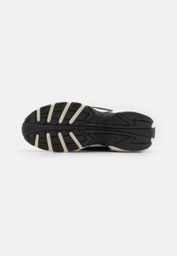 Black athletic shoe sole with a textured surface and distinct tread pattern. Features beige accents along the edges and grooves for traction.