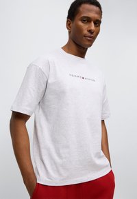 Γκρι κοντομάνικη μπλούζα με το λογότυπο «TOMMY HILFIGER» τυπωμένο με μαύρα γράμματα στο στήθος. Κατασ κευασμένη από απαλό βαμβακερό ύφασμα.